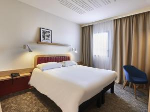 a hotel room with a large bed and a blue chair at ibis Styles La Roche-sur-Yon in Mouilleron-le-Captif