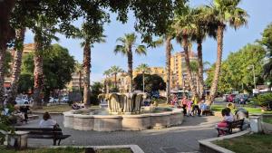 people sitting around a fountain in a park with palm trees at Ladispoli Apartment in Ladispoli +17 photos