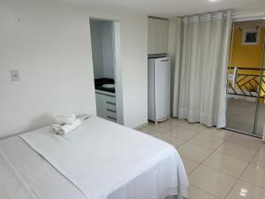 a bedroom with a white bed and a kitchen at El Shaday Suítes - ATÍNS in Atins