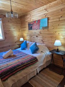 a bedroom with wooden walls and a bed with blue pillows at Cabañas Carolín Cacao Castaño in San José de Maipo
