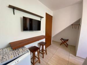 a kitchen with a tv on the wall and two stools at Kailua apartamentos e suítes in Porto De Galinhas