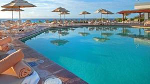 a swimming pool with chairs and umbrellas and the ocean at Beachfront Getaway Condo in Cancún