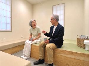 a man and woman sitting on a bench in a room at Apartment Hotel DIG the OSAKA in Suita