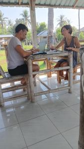 a man and a woman sitting at a table with a laptop at Dinoyin Bungalows in Gili Meno