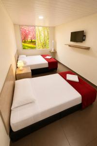 two beds in a small room with a tv at Hotel Arboleda de Cádiz in Ibagué