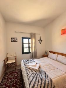 a bedroom with a bed and a chair and a window at Hôtel bleu ciel in Aït Yous