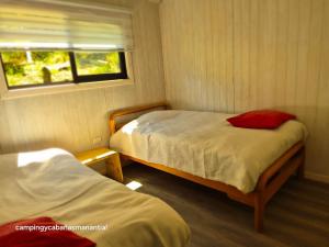 two beds in a small room with a window at cabañasmanantialpanguipulli in Panguipulli