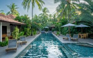 a pool at a resort with chairs and umbrellas at Belukar Villas in Gili Trawangan