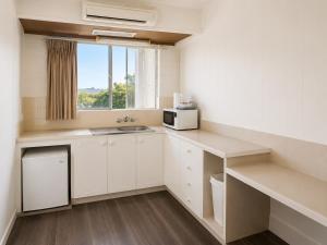 a small kitchen with white cabinets and a window at Forster Motor Inn in Forster