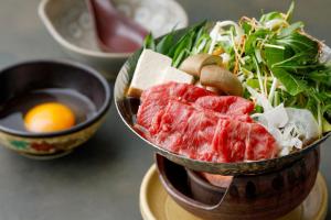 a bowl of food with meat and greens and an egg at Gion Ryokan Karaku in Kyoto