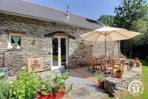 a stone cottage with a table and an umbrella at Le murmure des oiseaux in Plussulien