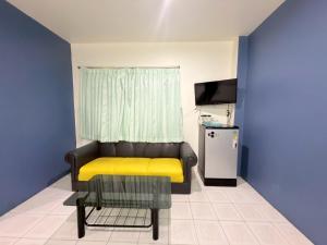 a living room with a yellow bench and a television at โรงแรม วี เฮาส์ ณ คอน in Nakhon Si Thammarat
