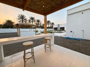 two stools at a bar in a backyard with palm trees at Etlaala Chalet in Ibri