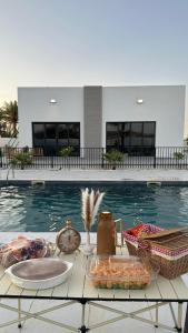 a table next to a swimming pool with food and a clock at Etlaala Chalet in Ibri