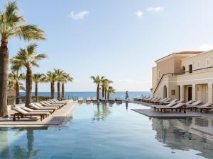 a swimming pool with chaise lounges and palm trees at Grecotel Marine Palace & Aqua Park in Panormos Rethymno