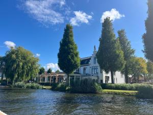 a white house with trees next to a river at Herberg Welgelegen in Katwijk
