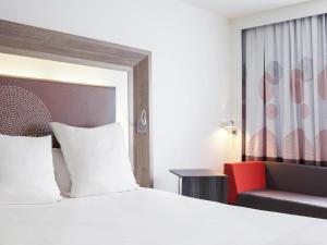 a hotel room with a bed and a red chair at Novotel Lille Aéroport in Lesquin
