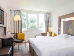 ein Hotelzimmer mit einem großen Bett und einem Schreibtisch in der Unterkunft Novotel Le Mans in Le Mans + 120 Fotos