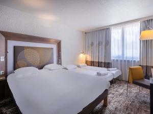 ein Hotelzimmer mit zwei Betten und einem Stuhl in der Unterkunft Novotel Le Mans in Le Mans