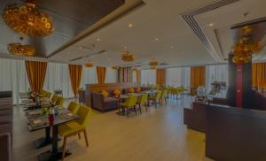 a living room with tables and chairs and a restaurant at Carnelian Muscat - Airport Hotel in Muscat