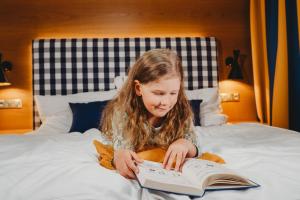 Ein kleines Mädchen sitzt auf einem Bett und liest ein Buch in der Unterkunft Hotel Bešeňová in Bešeňová