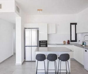 a white kitchen with two bar stools and a counter at Magical 4BR APT With Panoramic Sea View l Mamad in Bat Yam