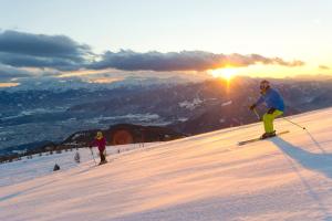 duas pessoas a esquiar numa encosta coberta de neve ao pôr-do-sol em Landhaus Gailer em Treffen