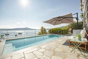 a swimming pool with a table and an umbrella at Lake House Lesa - Lakeside Villa Lago Maggiore in Lesa
