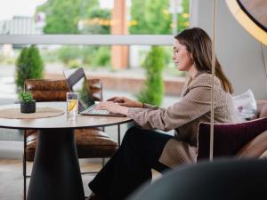a woman sitting at a table using a laptop at Hôtel Mercure Lille Aéroport in Lesquin