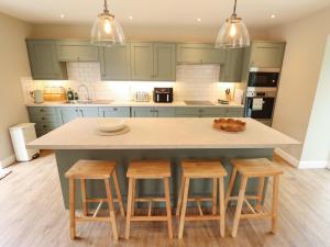 a kitchen with green cabinets and a island with stools at Bobblehat Barn in Alford