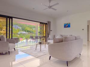 a living room with white furniture and a large window at Cove Holiday Apartments in Bel Ombre