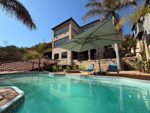 a swimming pool with an umbrella and chairs and a building at Khenjadji at Fish Eagle Bay in Bela-Bela