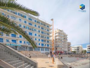 a large building on the beach with a palm tree at Apartamento Rocamar in S'Illot