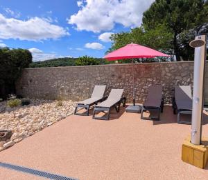 a group of chairs and an umbrella and a wall at Villa Le Nid du Pont d'Arc in Vallon-Pont-dʼArc