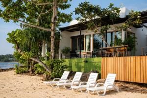 a row of chairs on the beach in front of a house at Ma's Sea Beach House in Klong Muang Beach