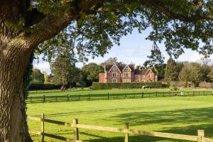 a large house in a field with a fence and a tree at Care Ashore Guest Rooms in Cranleigh