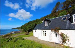 a white house on the side of a hill next to the ocean at The Kennels Ellary in Lochgilphead