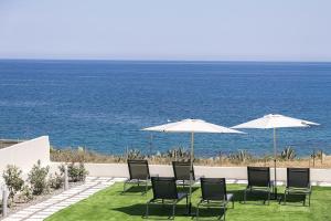a group of chairs and umbrellas on a lawn near the ocean at MGM Suites in Panormos Rethymno