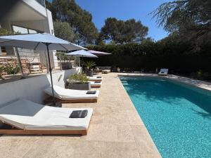 a pool with chairs and umbrellas next to a house at Villa "LES ALIZES" Côté jardin - Bord de mer in Saint-Raphaël