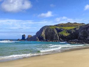 a beach with a rock formation in the ocean at Go Ye Cottage in Leurbost +28 photos