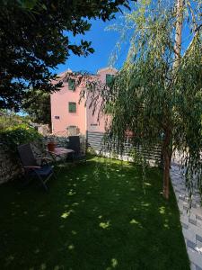 a yard with a table and a tree and a pink house at Apartman Donadina-Dalmatian heritage house in Trogir