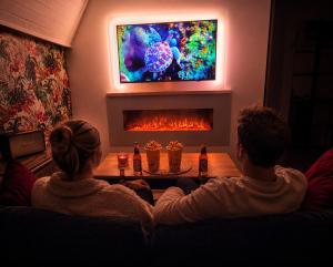 a man and woman sitting on a couch in front of a fireplace at MRODBNB - Appart Neuf - Vue Mer - 25m Plage & Resto - Ciné - cheminée - Popcorn in Cancale