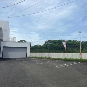 a parking lot with a white garage next to a fence at Lemon みやざき in Miyazaki