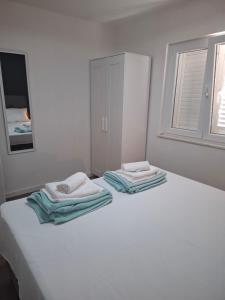 a white bed with two towels on top of it at Apartmani T'n'T in Pag