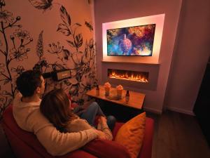 a man and woman sitting on a couch in front of a fireplace at MRODBNB - Maisonnette Atypique enfouie dans la Roche - Gr34, Plage, Resto & Huîtres à 25m in Cancale