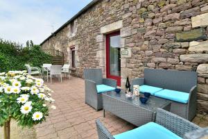 a patio with a table and chairs and a stone building at Les gites du buisson in Fréhel