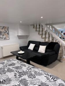 a living room with a black couch and stairs at Appartement Carreira in LʼIsle-Adam