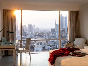a bedroom with a bed and a desk and a large window at Pullman Bangkok Hotel G in Bangkok