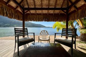 two chairs and a table on a beach with the water at Villa Ohana - 4BR Beachfront Villa in Paopao