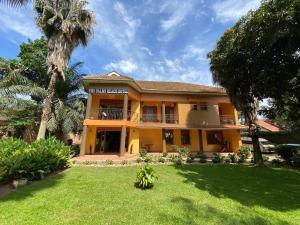 a yellow house with a palm tree and a yard at The Palms Beach Hotel and Restaurant in Entebbe